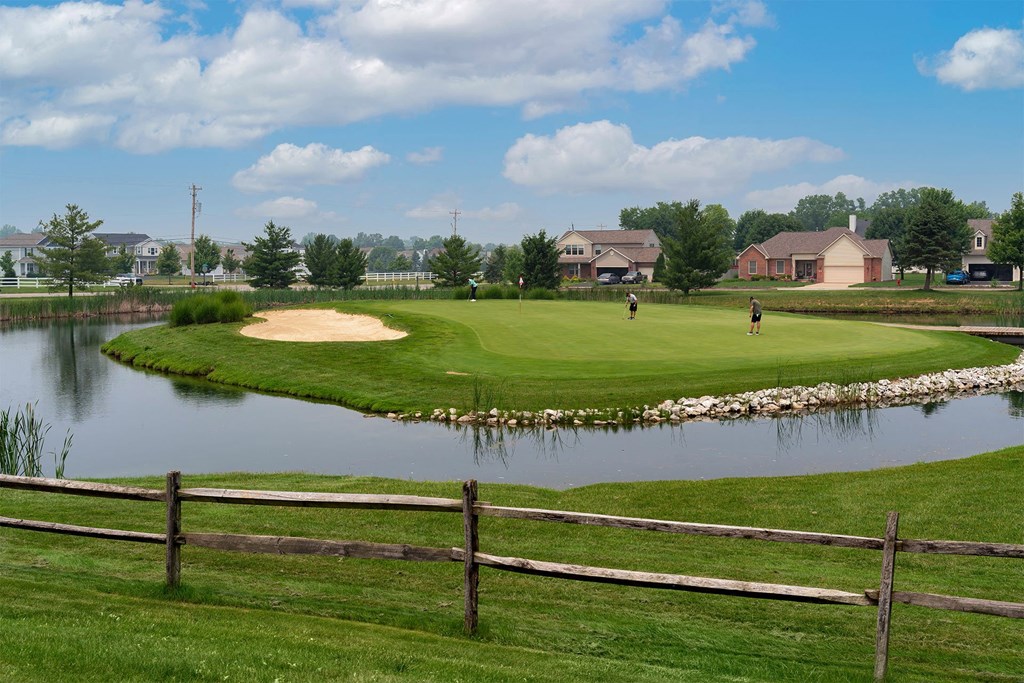 a golf course with a pond and houses in the background