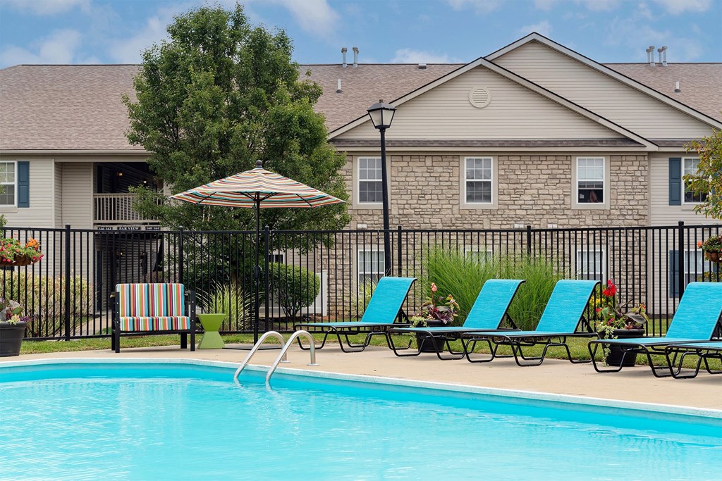 a swimming pool with blue chairs and an umbrella in front of a house