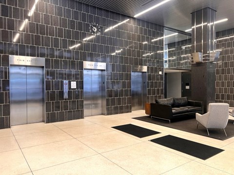 A modern waiting area with a black and white tiled wall and a wooden bench.
