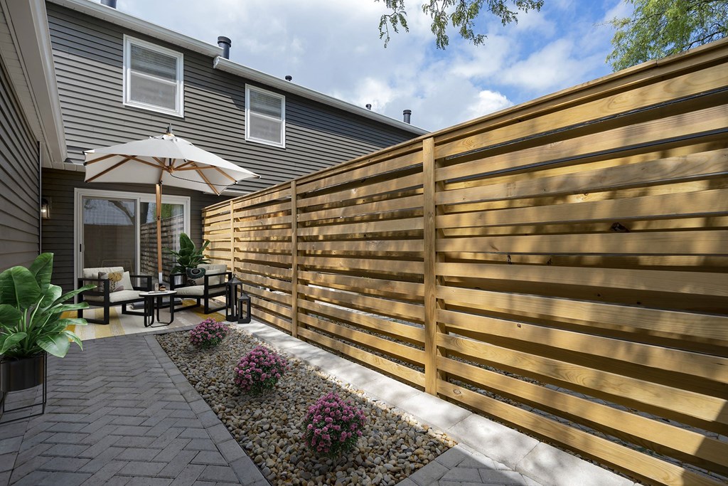 a wooden fence with horizontal slats separates a patio from a house