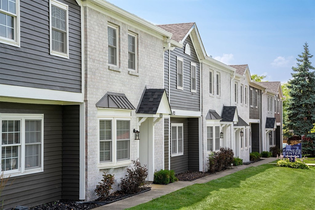 a row of townhomes with gray siding and a green lawn