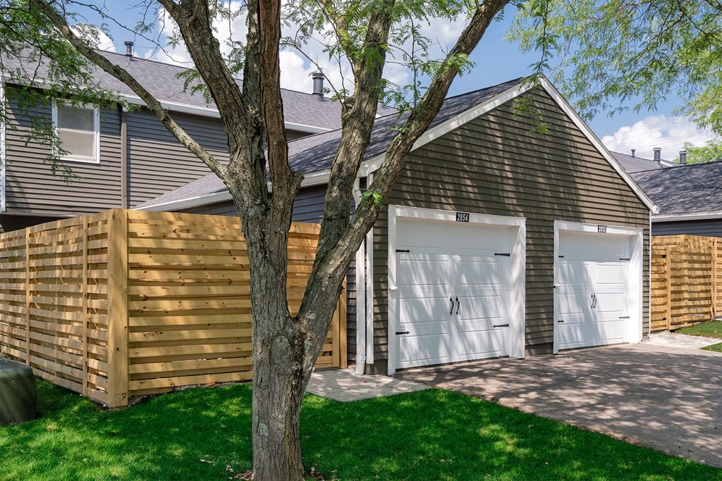 a detached garage with two white garage doors and a wood privacy fence