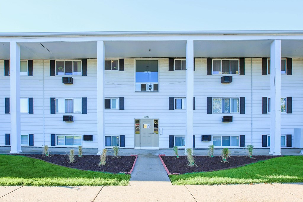 a white apartment building with a sidewalk and grass