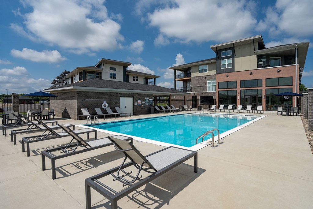 A swimming pool with sun loungers in front of a modern building.