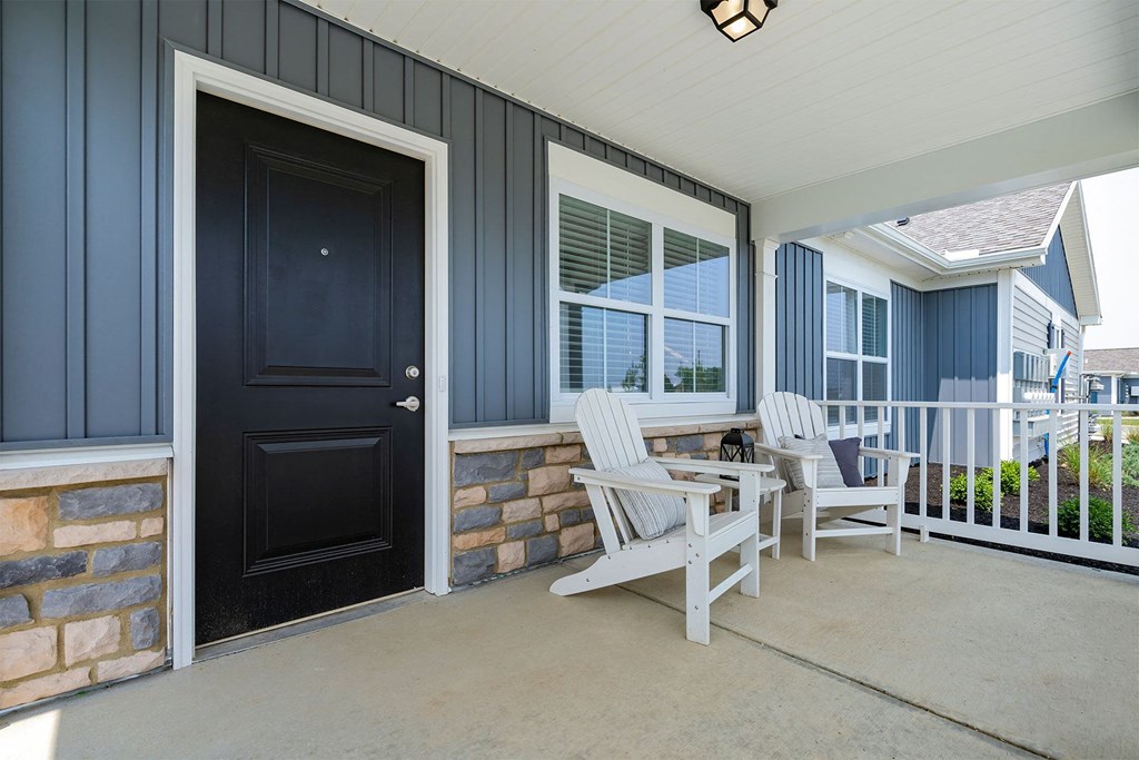 a front porch with two white rocking chairs and a small table