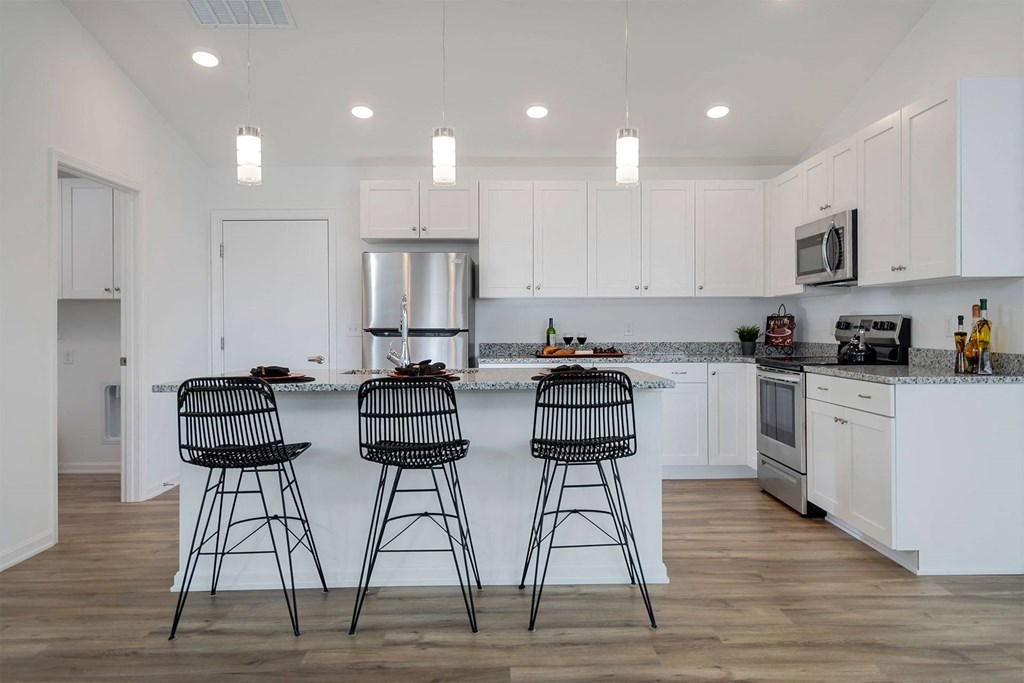 a kitchen with white cabinets and a large island with three bar stools in front of it