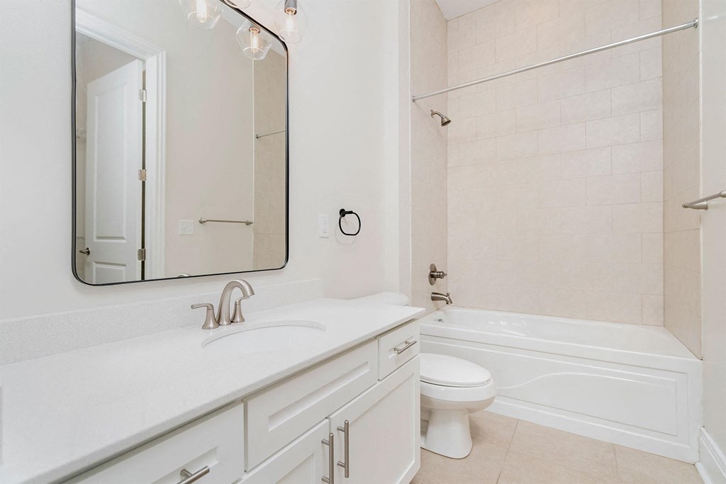 a bathroom with white cabinets and a white toilet next to a white bathtub with a shower