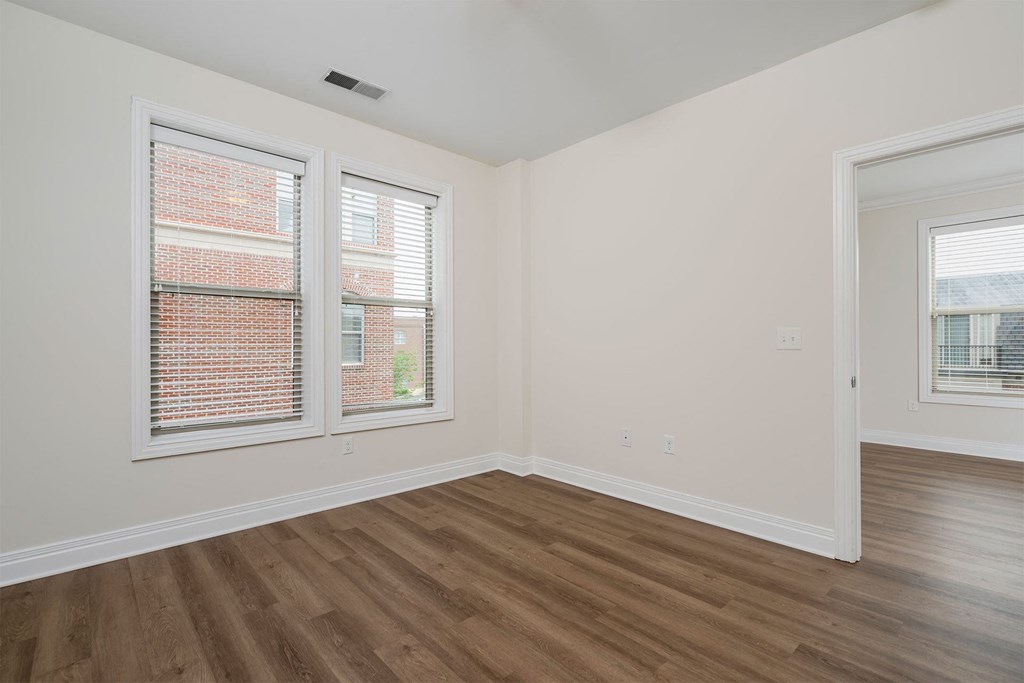 a bedroom with hardwood floors and two windows