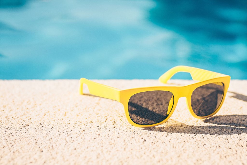 a pair of yellow sunglasses on the beach near a swimming pool