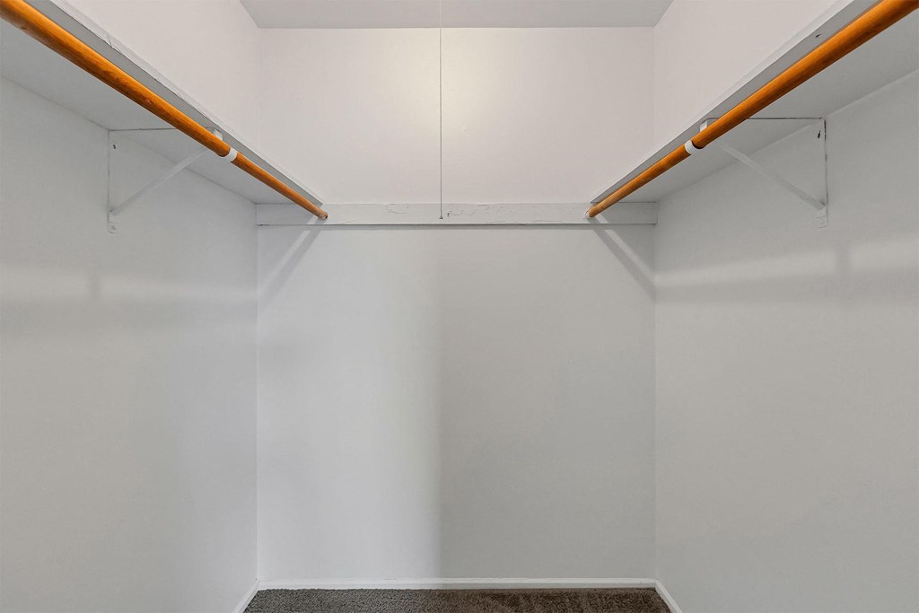 a walk in closet with white walls and two wooden rods hanging from the ceiling