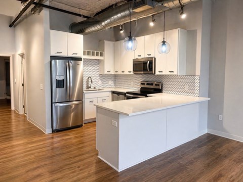 A modern kitchen with a stainless steel refrigerator and wooden floors.