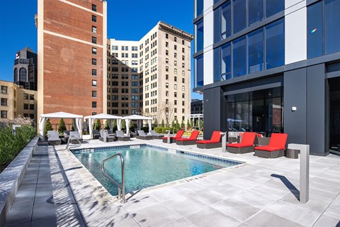 A pool surrounded by red chairs and umbrellas.