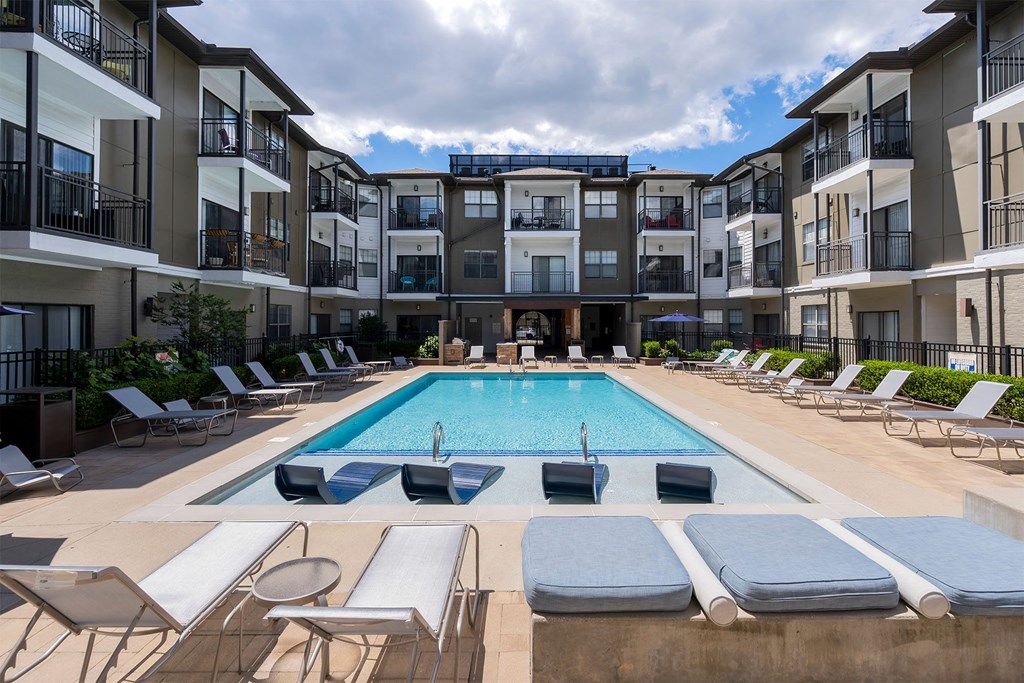 a swimming pool with lounge chairs in front of an apartment building