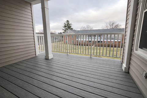 A wooden deck with a white railing and a view of a building in the distance.