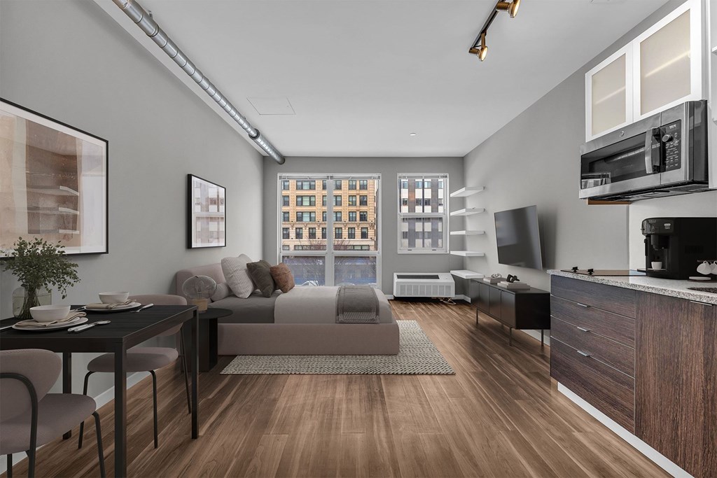 A modern kitchen with a dining table and chairs in the foreground and a living room with a couch and a window view in the background.