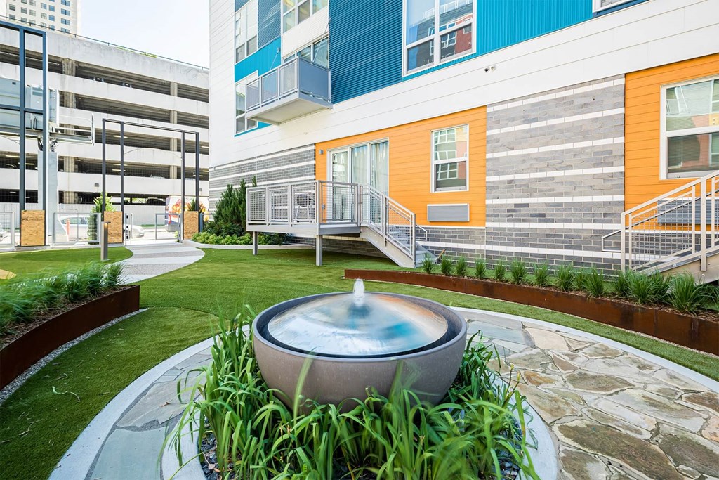 A modern building with a blue and orange exterior and a circular fountain in the foreground.