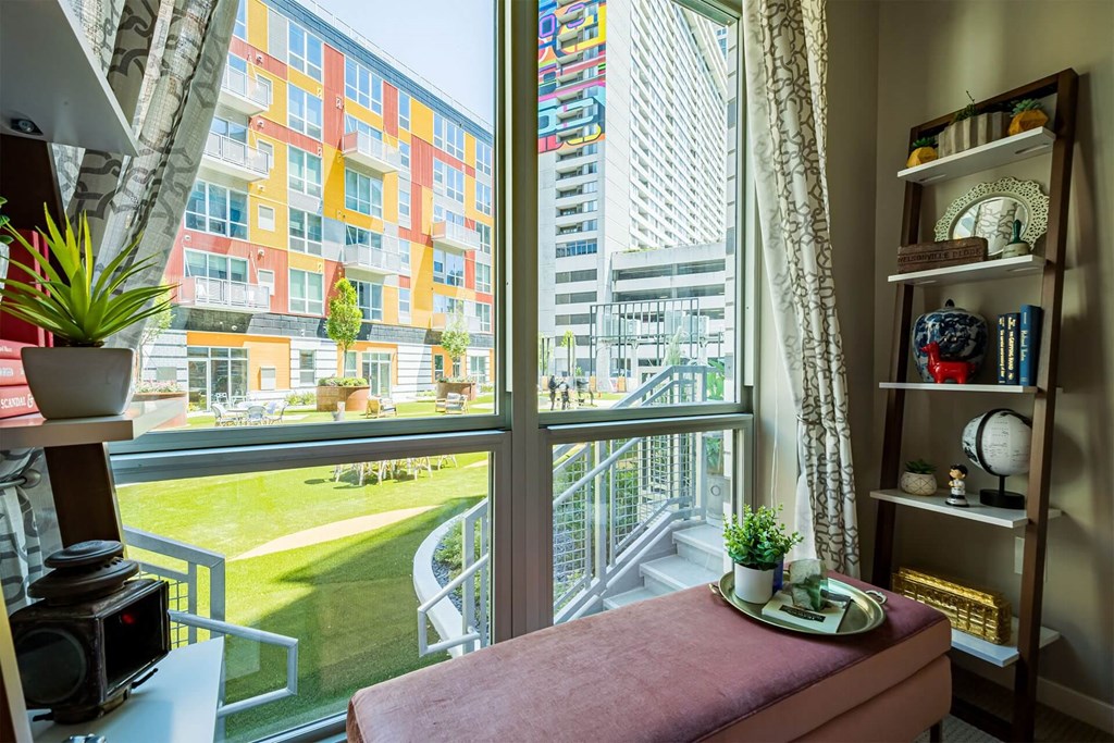 A room with a window overlooking a courtyard with a bench and a table with a plant on it.
