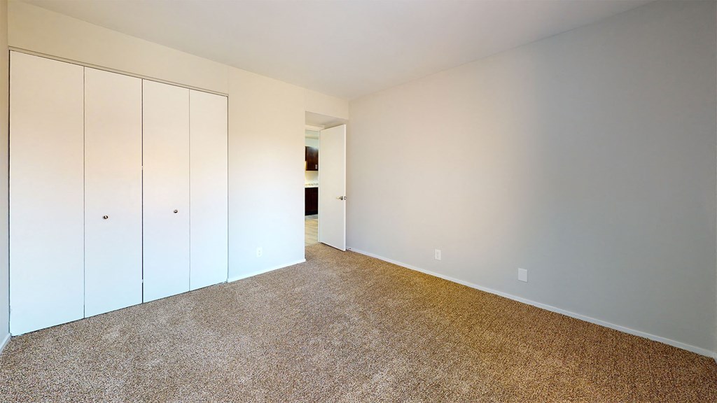 a bedroom with white walls and carpet and closet space