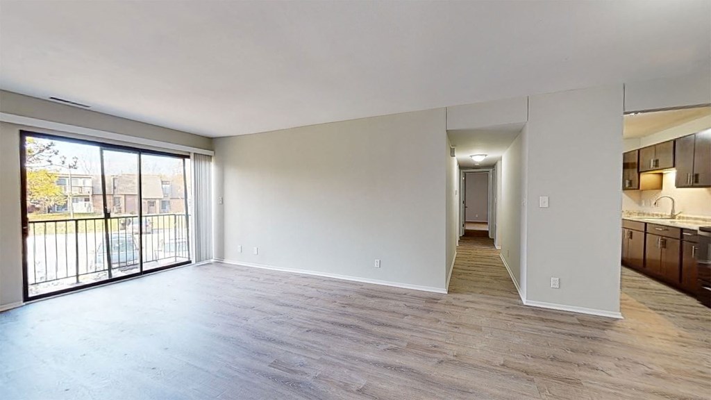 an empty living room with a sliding glass door to a kitchen