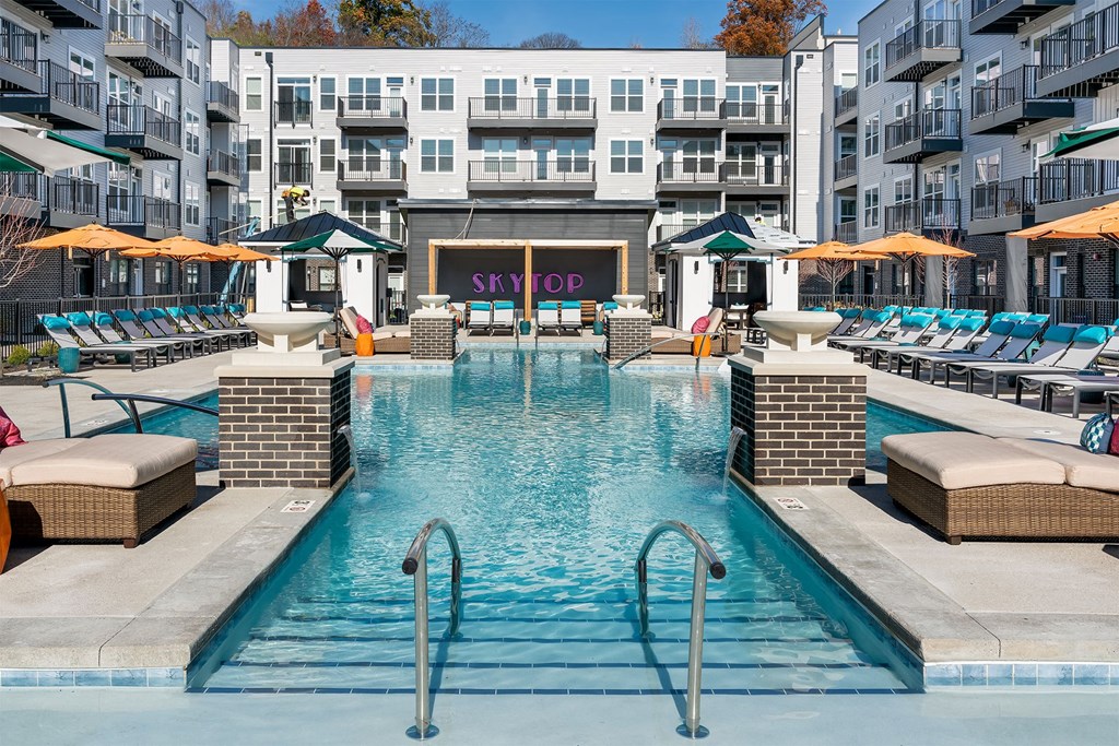 a swimming pool at an apartment building with chairs and umbrellas