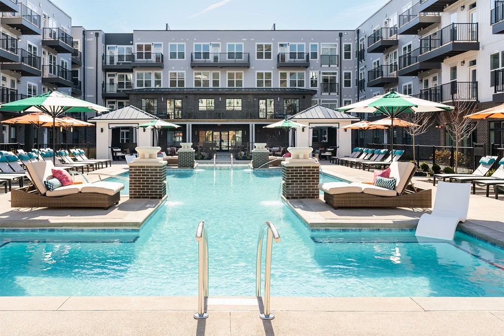 a swimming pool with chairs and umbrellas in front of an apartment building