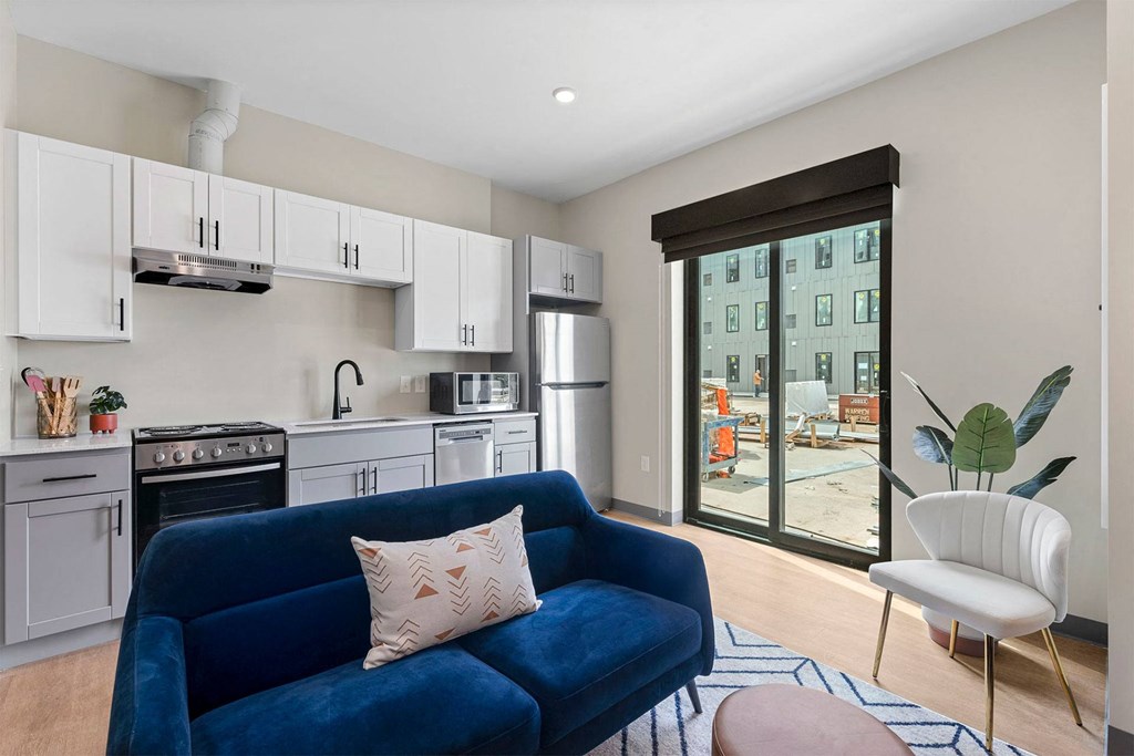 a living room with a blue couch and a kitchen with white cabinets and stainless steel appliances