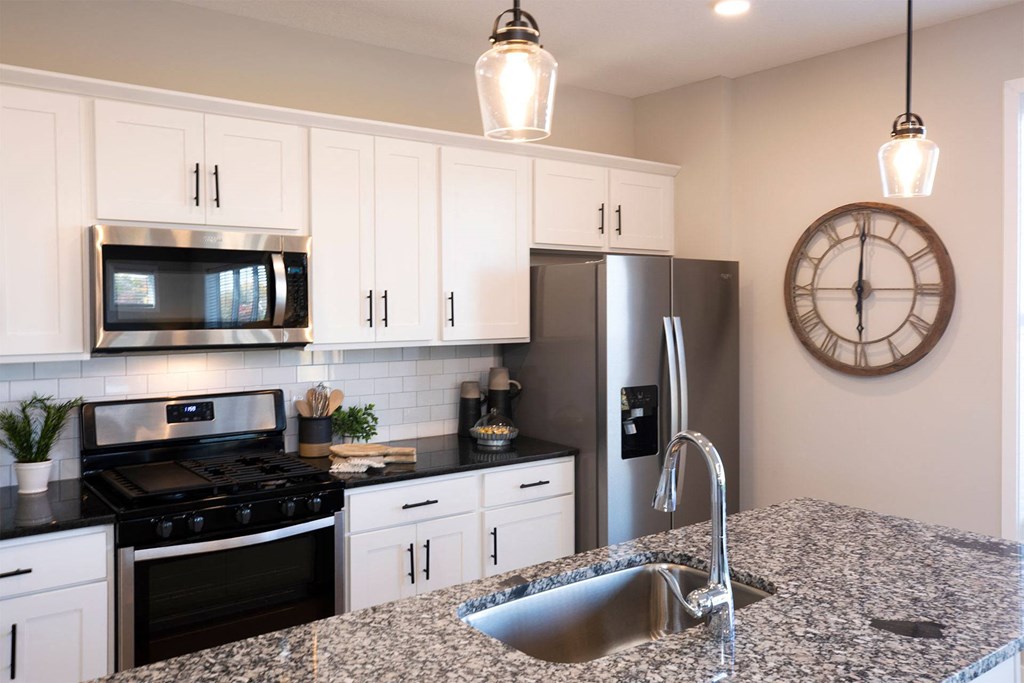 a kitchen with white cabinets and a large clock on the wall