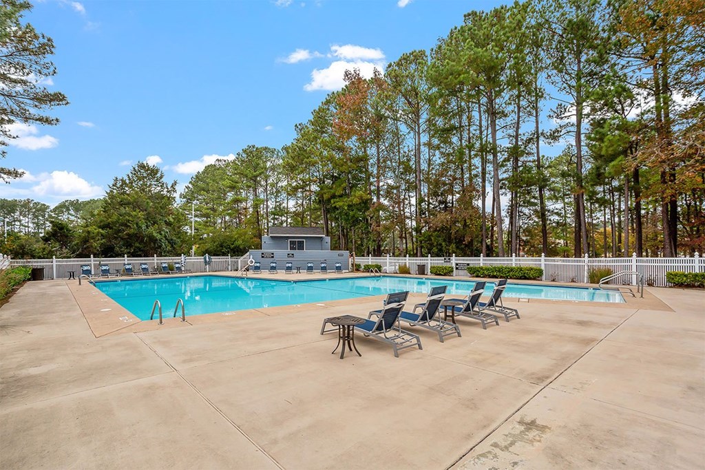 A swimming pool surrounded by trees and chairs.