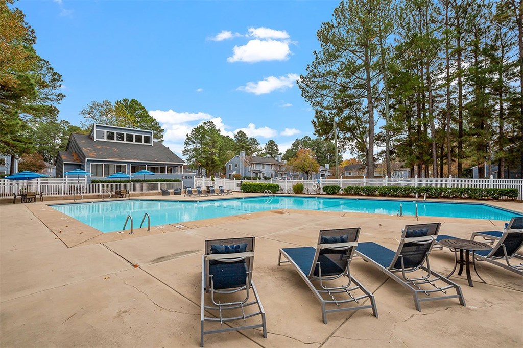 A pool surrounded by trees and chairs.