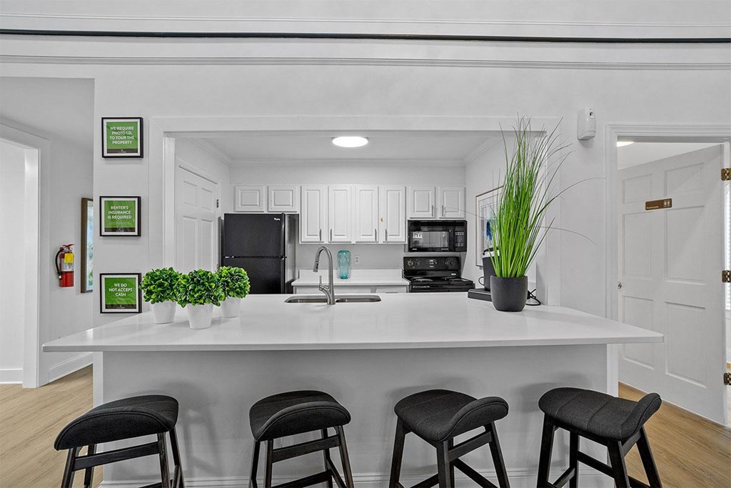 A kitchen with white cabinets and a white island with three black stools.