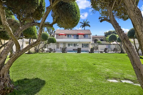 A house with a red roof is surrounded by a green lawn and trees.