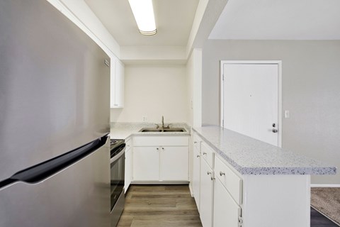 A kitchen with a refrigerator on the left and a sink with a countertop on the right.