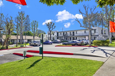 A sunny day at the Heritage Apartments with cars parked and trees in the background.