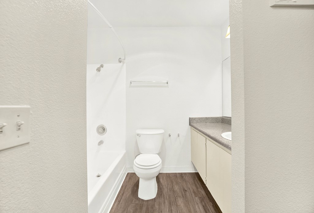A white toilet in a small bathroom with a wooden floor.