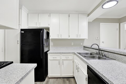 A black refrigerator sits in a kitchen with white cabinets and a granite countertop.