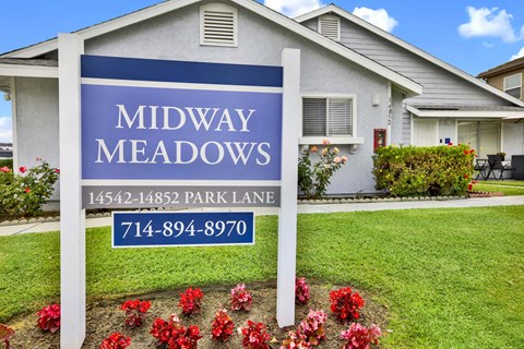 A sign for Midway Meadows with a house in the background.