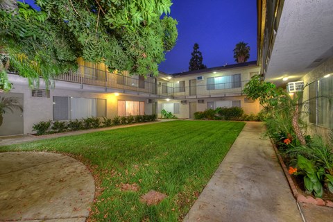A well-lit apartment complex with a green lawn and trees.