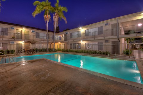 A swimming pool surrounded by apartment buildings at night.