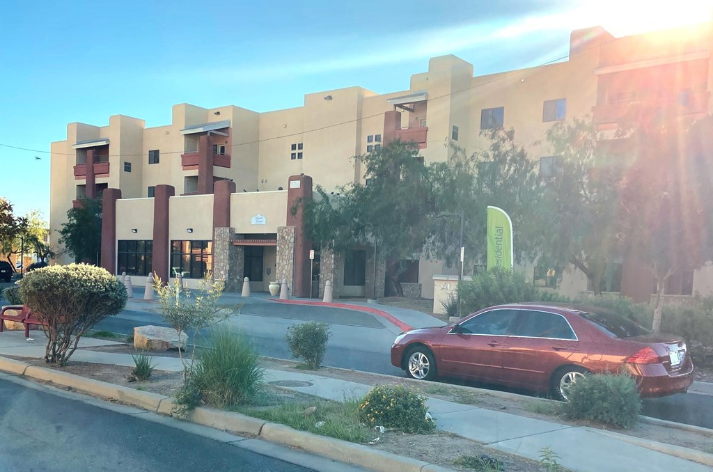A red car is parked on the side of the road in front of a building.