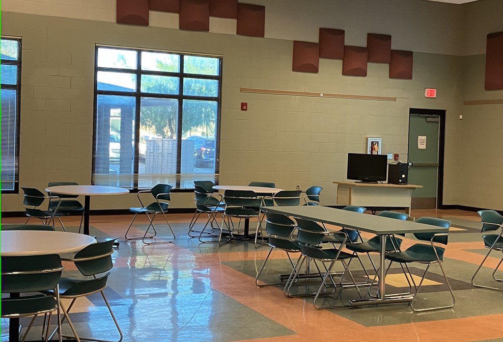 A room with tables and chairs and a TV on a stand.