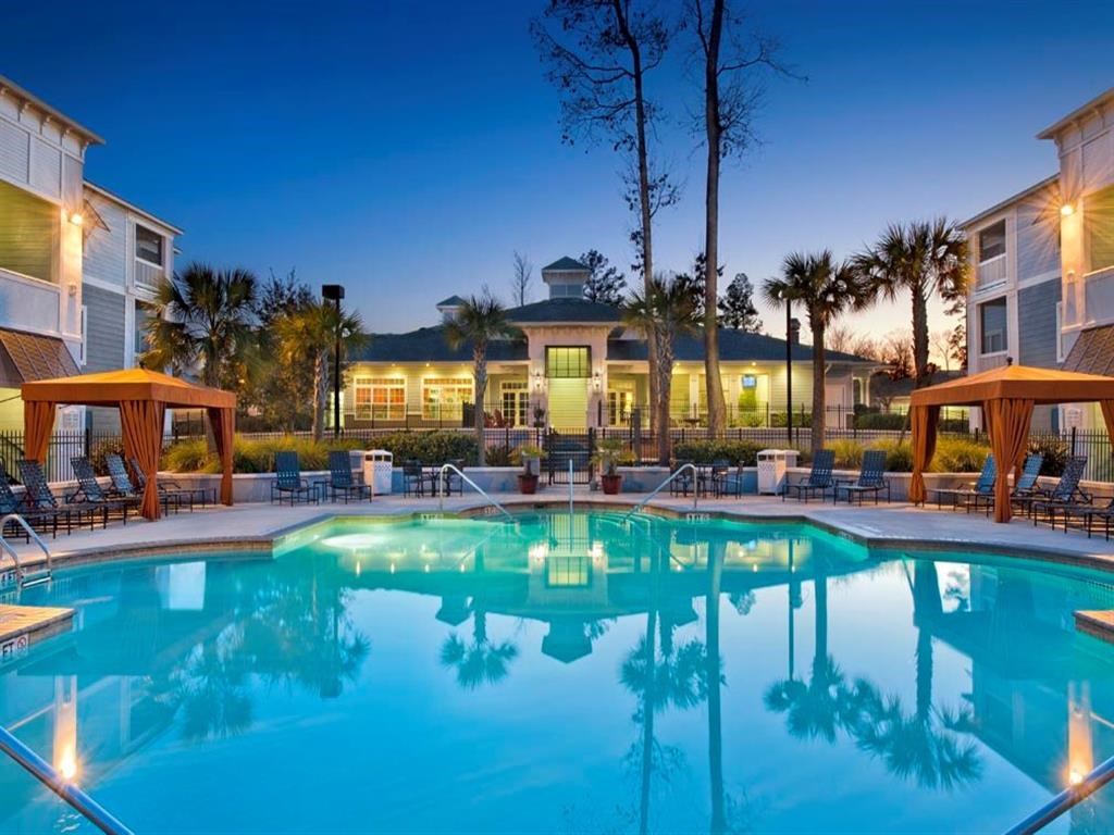 A swimming pool in front of a building with lights on.
