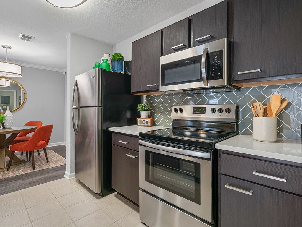 A modern kitchen with a stainless steel refrigerator, microwave, oven, and a tile backsplash.