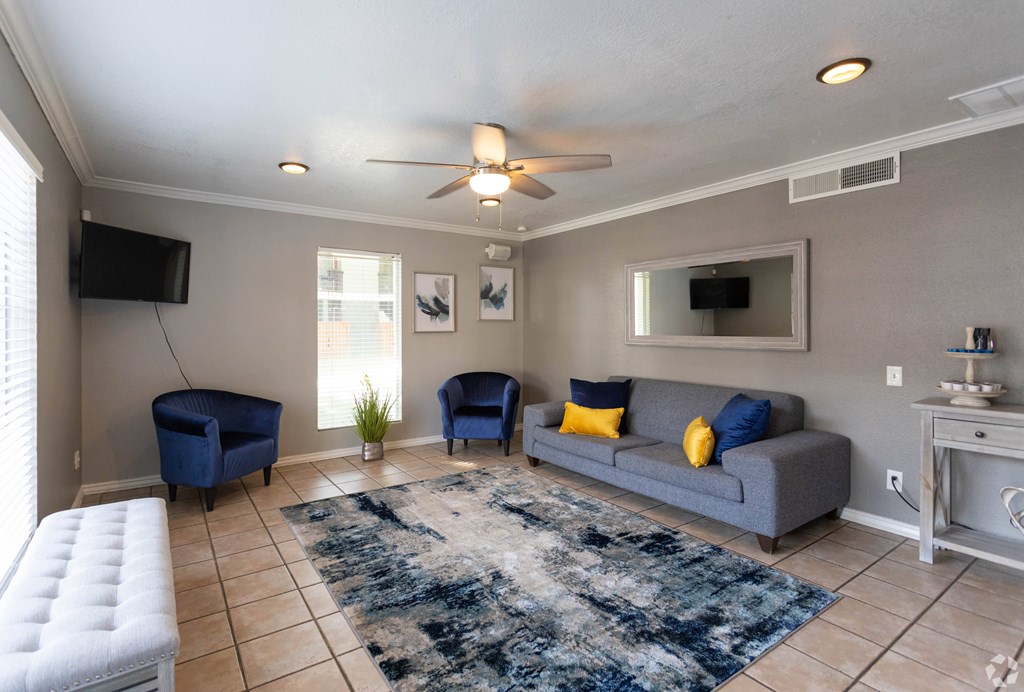 A living room with a grey couch, blue chairs, and a white ottoman.