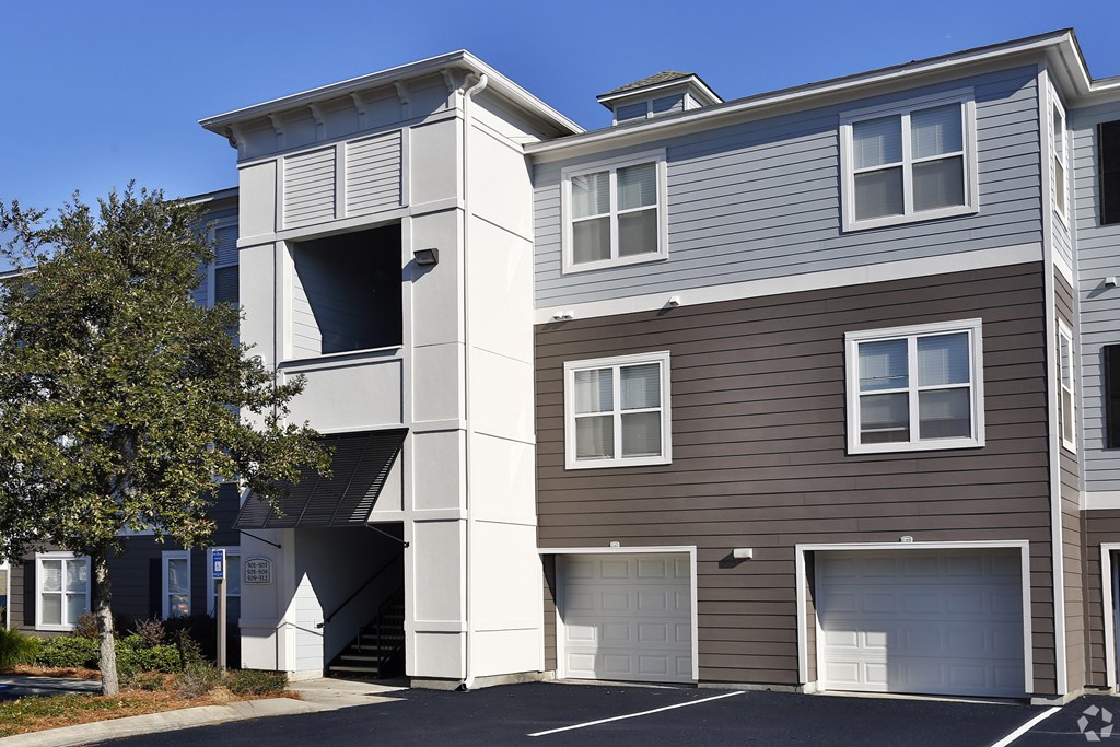 A modern two-story residential building with a parking lot in front.