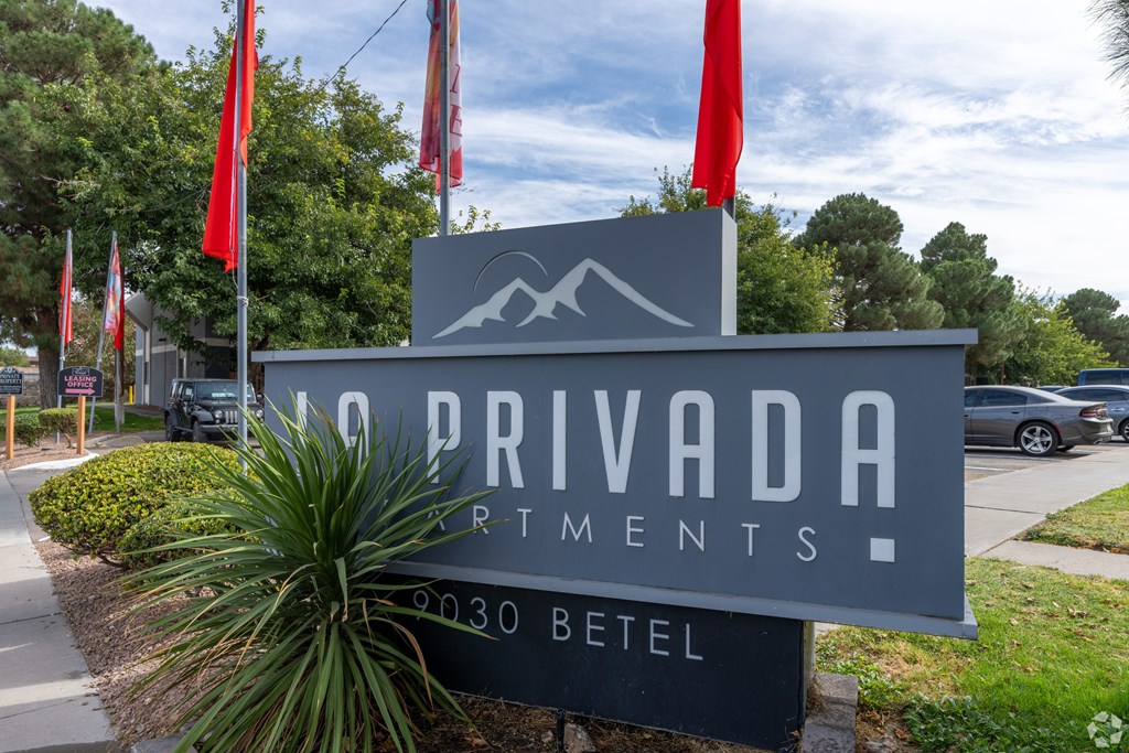 A sign for Privada Artments stands in front of a tree.