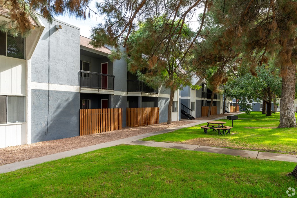 A building with a red door and a balcony is surrounded by trees and a picnic table.