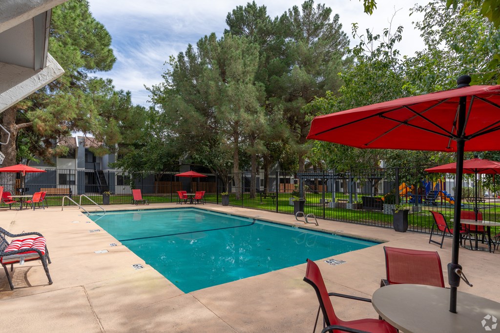 A pool area with red chairs and umbrellas.