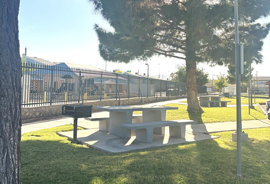 A concrete picnic table is in the middle of a grassy area.