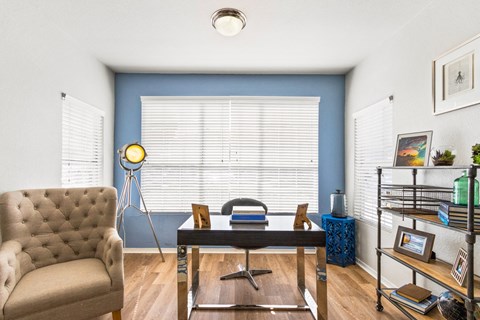 a living room with a blue wall and a window and a desk with a chair