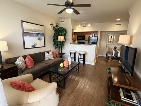 A living room with a brown couch, a white chair, and a painting on the wall.